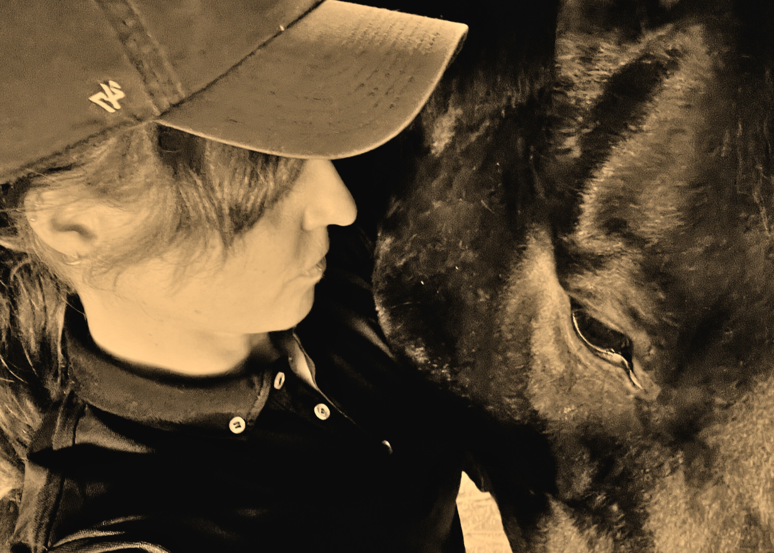 Person wearing a cap and jacket interacting with a horse in a sepia-toned photo.